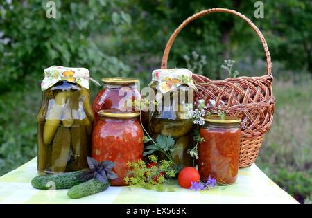 Les conserves maison (concombres, tomates, salade de légumes) avec jardin en arrière-plan. Banque D'Images