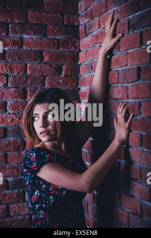 Scared young woman standing in coin de mur de briques et à l'écart Banque D'Images