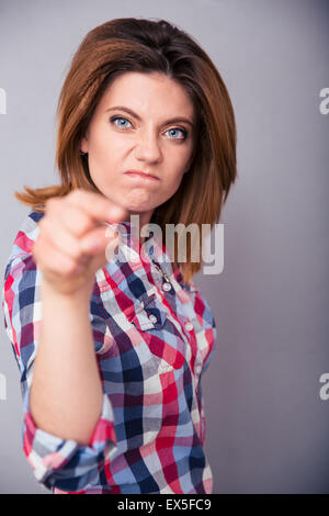 Jeune femme en colère pointant à huis clos sur fond gris Banque D'Images