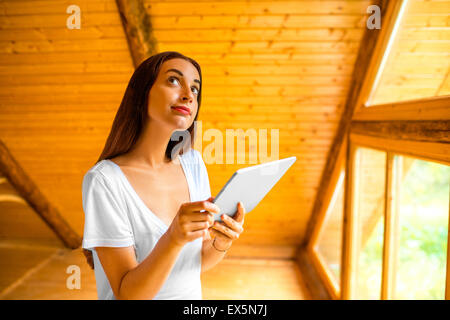 Woman thinking with digital tablet in la maison en bois Banque D'Images