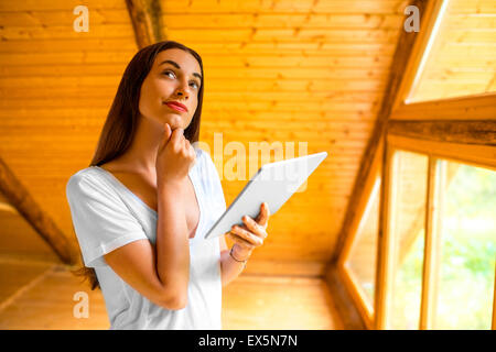 Woman thinking with digital tablet in la maison en bois Banque D'Images