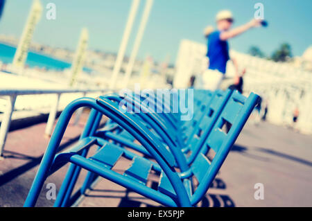 Vue sur la caractéristique de chaises bleues face à la Méditerranée sur la Promenade des Anglais à Nice, France, et un flou Banque D'Images