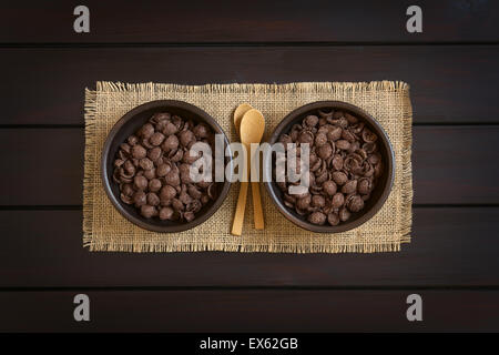 Chocolat croustillant flocons de maïs céréales petit déjeuner dans des bols rustiques avec de petites cuillères en bois, photographié dans le ciel en bois Banque D'Images