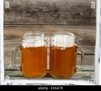 Voir à travers les fenêtres de deux pots de verre remplis de frosty bière froide sur le dessus de caisse en bois rustique en bois avec en arrière-plan. Banque D'Images