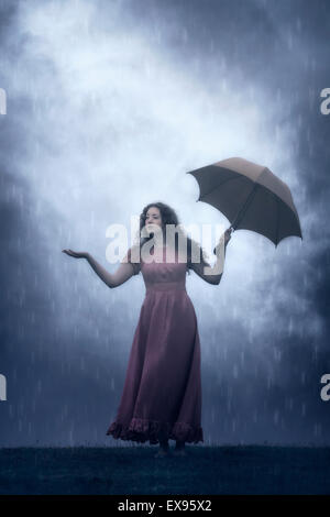 Une femme dans une robe rose avec un parapluie sous la pluie Banque D'Images