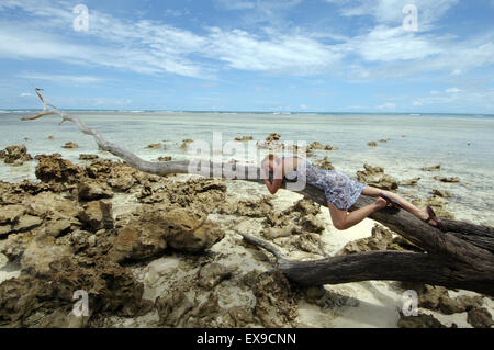 Jeune femme dormir sur un tronc d'arbre tombé, sur les rives de l'Océan Indien, Banque D'Images