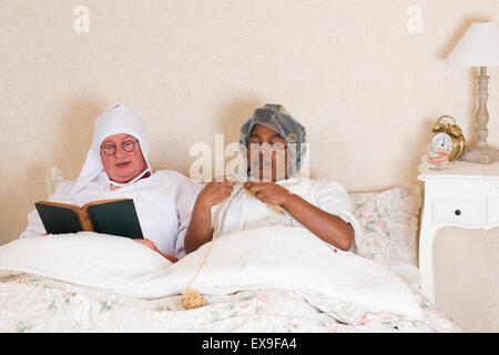 Couple de personnes âgées dans la lecture et vêtements vintage knitting in bed Banque D'Images