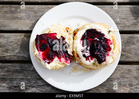 Un Scone anglais traditionnel coupé en deux et étalé avec de la crème et de la confiture. Fait partie d'un thé à la crème anglais traditionnel servi à l'extérieur Banque D'Images