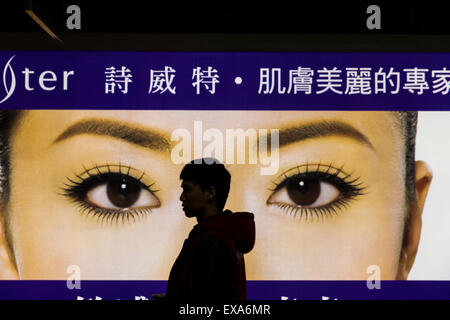 En Asie, Taiwan, Taipei, Silhouette de jeune homme en passant devant des panneaux lumineux les yeux de femme chinoise à l'intérieur de la station de métro MTR de Taipei Banque D'Images