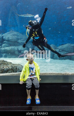 En Asie, Singapour, jeune garçon pose pour les snapshots instantanés en face de scuba diver en natation à l'intérieur du réservoir requin massif S.E.A. Banque D'Images