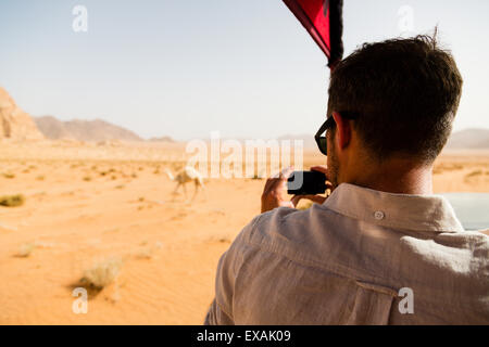 Wadi Rum, Jordanie. L'homme portant des lunettes de soleil en prenant une photo d'un chameau d'un camion safari. Banque D'Images