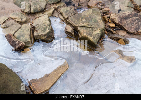 Close up detail rock l'érosion. Pierre meulière érodé avec petites fissures et les pierres dans la glace du cours d'eau gelés. Kinder Scout, Derbyshire, Royaume-Uni Banque D'Images