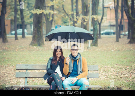 Jeune couple dans le parc durant la saison d'automne en plein air - saint valentin amoureux sous égide assis dans un banc Banque D'Images