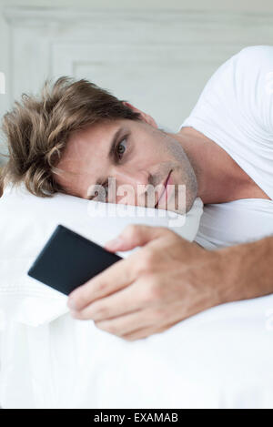 Man Lying in Bed using smartphone Banque D'Images