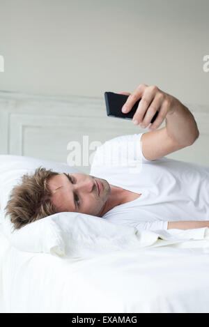 Man using smartphone on bed Banque D'Images