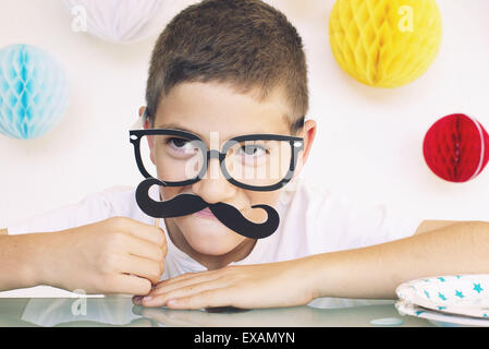 Boy wearing fake moustache et lunettes à un anniversaire, portrait Banque D'Images