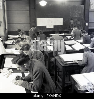 années 1950, historique, un groupe de jeunes apprentis ingénieurs masculins dans une salle de classe qui font du dessin technique à des bureaux en bois individuels traditionnels, avec deux enseignants ou instructeurs masculins sur un grand tableau noir, dont un qui donne de l'aide à un étudiant. Banque D'Images