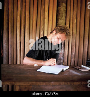 Village Pavuru, au Brésil. Sting écrit à une table dans une maison indienne ; zone indigène du Xingu (Brésil), novembre 1990. Banque D'Images