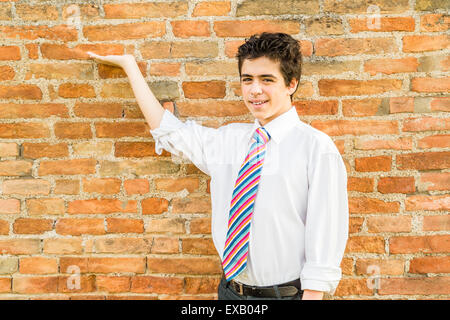 Handsome Young boy portant une chemise blanche et une cravate régimentaire de rouge, fuchsia, orange, bleu, indigo et white stripes est montrant en face d'un mur de briques au coucher du soleil Banque D'Images