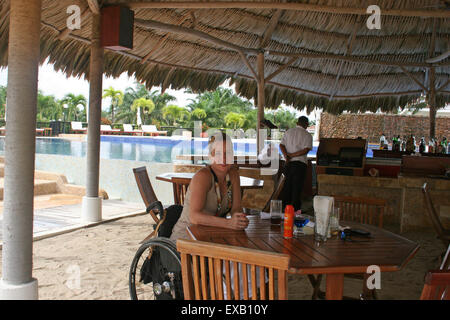 Femme à l'aide d'un fauteuil roulant à un bar de piscine à Belize Banque D'Images