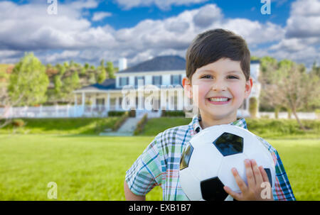 Cute Smiling Young Boy Holding Soccer Ball en face de belle maison. Banque D'Images