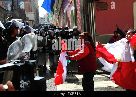 La Paz, Bolivie, 10 juillet 2015. Un manifestant de la région de Potosi affronte la police anti-émeute lors d'une manifestation organisée par le Comité civique de Potosi et ses partisans. Ils sont à la Paz pour exiger que le gouvernement tienne les promesses électorales faites à la région dans le passé. La police a utilisé des gaz lacrymogènes pour empêcher les manifestants d'entrer sur la Plaza Murillo (en arrière-plan, où se trouvent le Palais présidentiel et les bâtiments du Congrès). Les drapeaux rouge et blanc sont les drapeaux du département de Potosí. Crédit : James Brunker / Alamy Live News Banque D'Images