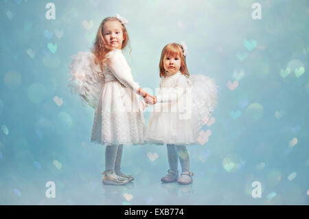 Deux petites filles habillées comme des anges en blanc sur un fond bleu studio Banque D'Images