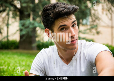 Portrait Jeune homme à l'écoute de sa musique préférée en utilisant la prise casque au parc. Banque D'Images