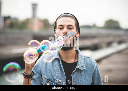 Beau jeune homme hipster barbu faisant des bulles de savon dans la ville Banque D'Images