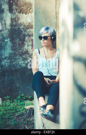 De beaux cheveux bleus courte femme hipster au casque de la musique dans la ville Banque D'Images