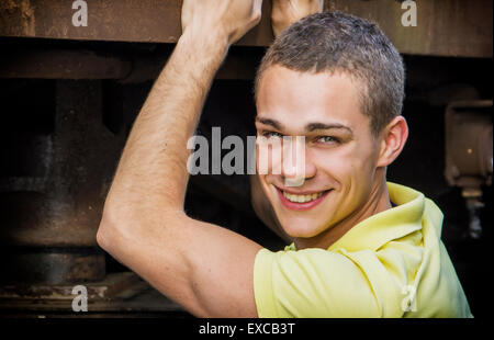 Beau jeune homme appuyé contre old rusty metal, extérieur, smiling and looking at camera Banque D'Images