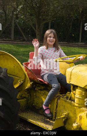 Un modèle publié jeune fille de 9 ans jouant et en agitant sur un tracteur au cours d'une ferme dans le Bedfordshire. Banque D'Images