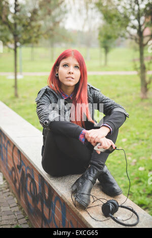 Belle jeune femme vénézuélienne de cheveux rouge de vie dans la ville de Milan, rue de plein air à l'écoute de la musique avec des écouteurs Banque D'Images