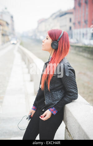 Belle jeune femme vénézuélienne de cheveux rouge de vie dans la ville de Milan, rue de plein air à l'écoute de la musique avec des écouteurs Banque D'Images