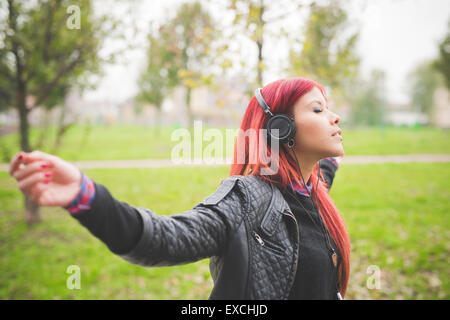 Belle jeune femme vénézuélienne de cheveux rouge de vie dans la ville de Milan, rue de plein air à l'écoute de la musique avec des écouteurs Banque D'Images