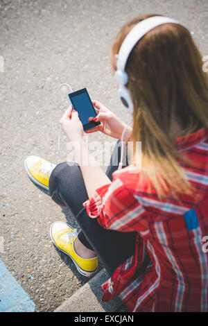 Belle blonde jeune hipster femme dans la ville d'écouter de la musique avec des écouteurs et smartphone Banque D'Images