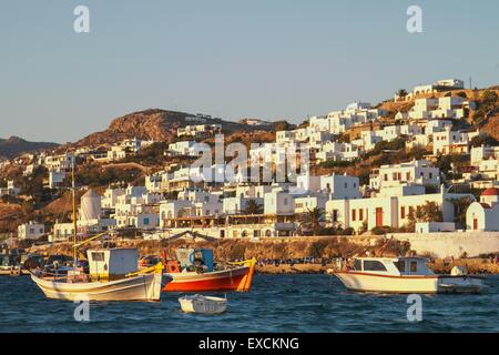 Coucher du soleil à Mykonos, Grèce. Bateaux en premier plan et merveilleuse lumière orange hits les maisons sur la côte hill Banque D'Images