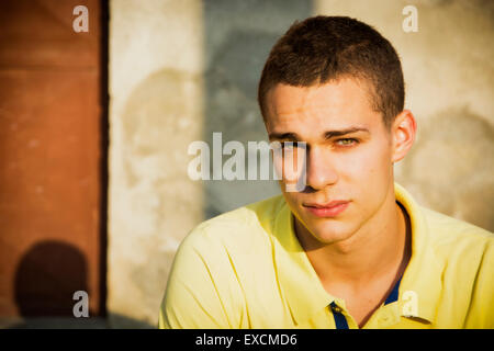Beau jeune homme aux yeux verts appuyé contre un mur de béton, looking at camera Banque D'Images