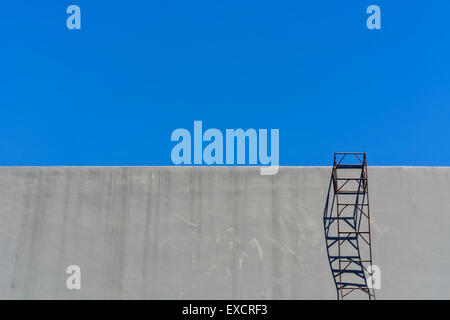 Sur l'échelle de l'acier contre mur gris ciel bleu sans nuages, Banque D'Images