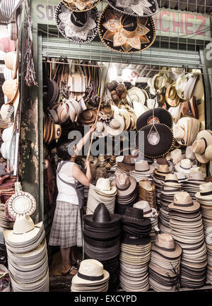 Une femme ayant atteint avec mât pour accrocher des sombreros mexicains comme elle ouvre son petit chapeau décroche à un marché Mexicain Banque D'Images