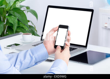 À l'aide de main d'hommes maquette Smartphone avec écran blanc au bureau bureau avec un ordinateur portable et tablette ordinateur maquette. Banque D'Images