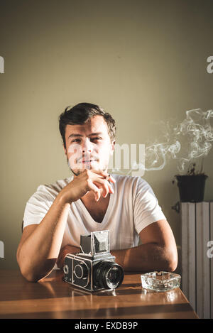 Jeune homme élégant hipster avec ancien appareil photo sur la table à la maison Banque D'Images