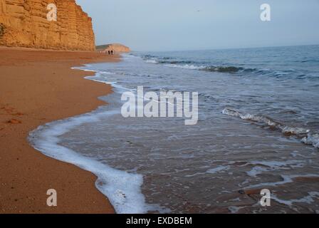 Vagues qui surplombent doucement la plage sous les falaises de grès de West Bay, Dorset, Royaume-Uni Banque D'Images