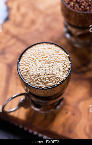 Le quinoa brut blanc dans une tasse en verre, le quinoa rouge à l'arrière, olive wood background, selective focus, vue du dessus Banque D'Images