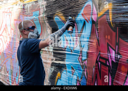 Un graffiti artiste utilise un aérosol de peinture sur un mur à peindre une image Banque D'Images