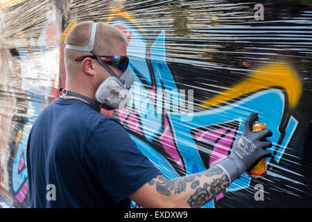 Un graffiti artiste utilise un aérosol de peinture sur un mur à peindre une image Banque D'Images