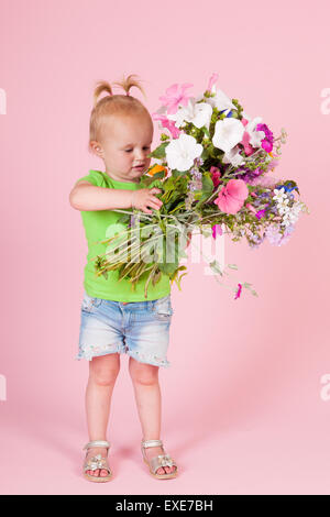 Portrait bébé fille avec bouquet de fleurs du jardin sur fond rose Banque D'Images