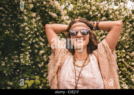 Hippy-longs à la jeune femme en blouse blanche et châle tricoté debout parmi les fleurs Banque D'Images