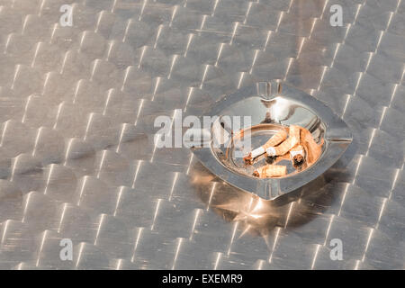 Les cogné mégots de cigarettes filtres dans un cendrier en acier inoxydable à l'extérieur sur une table en métal. Fumeurs concept conceptuel Banque D'Images