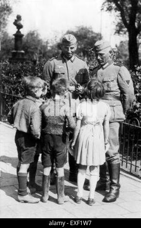 Une photographie de la seconde Guerre mondiale montrant des soldats allemands en conversation avec des enfants. Cette image capture un moment d'interaction au milieu des dures réalités de la guerre, donnant un aperçu de l'expérience civile au cours de cette période tumultueuse. Banque D'Images